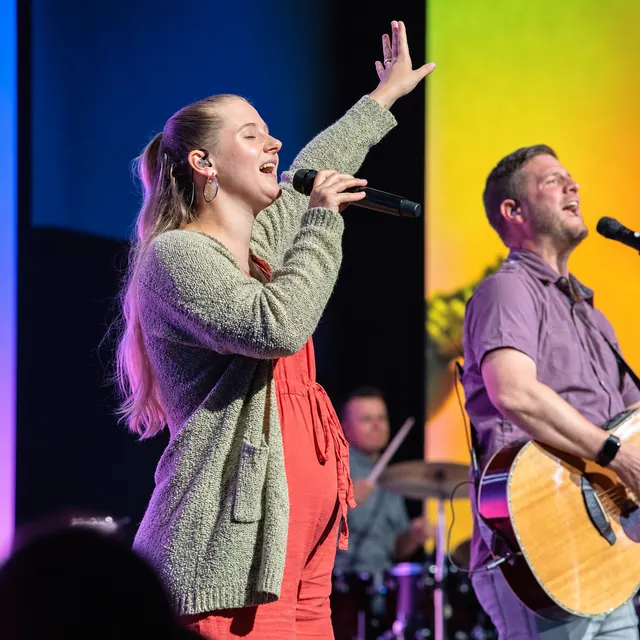 Worship leader singing on a warmly lit stage